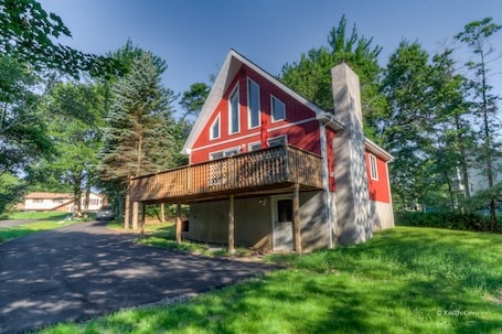A red house with a balcony, surrounded by trees and a clear sky.