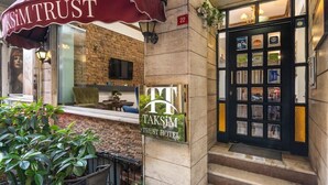 The exterior of the TaksiM Trust Hotel, featuring a brick facade, a black door with glass panels, and a red awning with the hotel's name. - Taksim Trust Hotel (Istanbul)