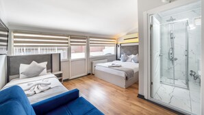 A modern hotel room with a large bed, a separate sofa, a glass shower enclosure, and a view of the city through the windows. - Taksim Trust Hotel (Istanbul)