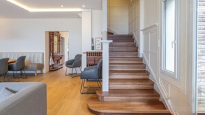 A modern living room with a wooden staircase, a seating area with sofas and chairs, and a view of the upper floor.