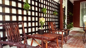 A wooden outdoor seating area with chairs and a table, a potted rose, and a lattice wall.