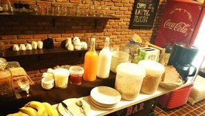 A breakfast bar with various food items and beverages, including bananas, bread, and a Coca-Cola sign. - The Hostel 16 (Bangkok)