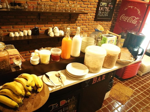 A breakfast bar with various food items and beverages, including bananas, bread, and a Coca-Cola sign. - Hostel 16 (Bangkok)