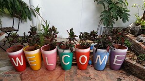 A row of potted plants with letters spelling "WELCOME" on the pots, placed on a tiled patio. - Hostel 16 (Bangkok)