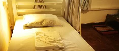 A bed with white linens, a wooden headboard, and curtains tied back at the window.