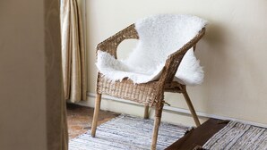 A wicker chair with a white fluffy throw, placed on a patterned rug in a room with a tiled floor and a plain wall. - The Hostel 16 (Bangkok)