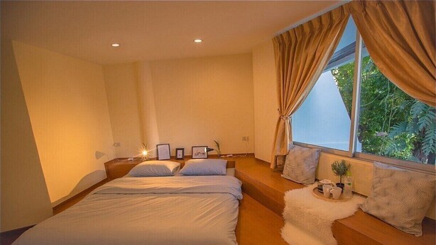 A bedroom with a large bed, a window with curtains, and a small table with decorative items. - The Hostel 16 (Bangkok)