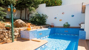 Una piscina con azulejos azules, un muro de piedra y un banco.