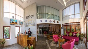 A hotel lobby with a reception desk, a seating area with a sofa and chairs, a large wall with a clock and a sign reading "Le Cocor Boutique Hotel". - Le Cocon Boutique Hotel (Phnom Penh)