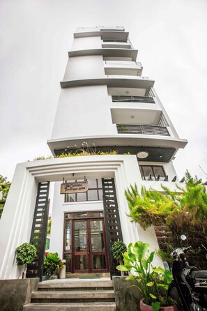 A tall, white building with a unique stepped design, featuring a sign for 'The Cocoon Boutique Hotel' at the entrance.
