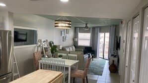 A modern kitchen with a refrigerator, stove, and sink. There is a dining area with a table and chairs, and a living room with a sofa and a TV. - Modern Beach Condo ON  St. Pete Beach! (St. Pete Beach)