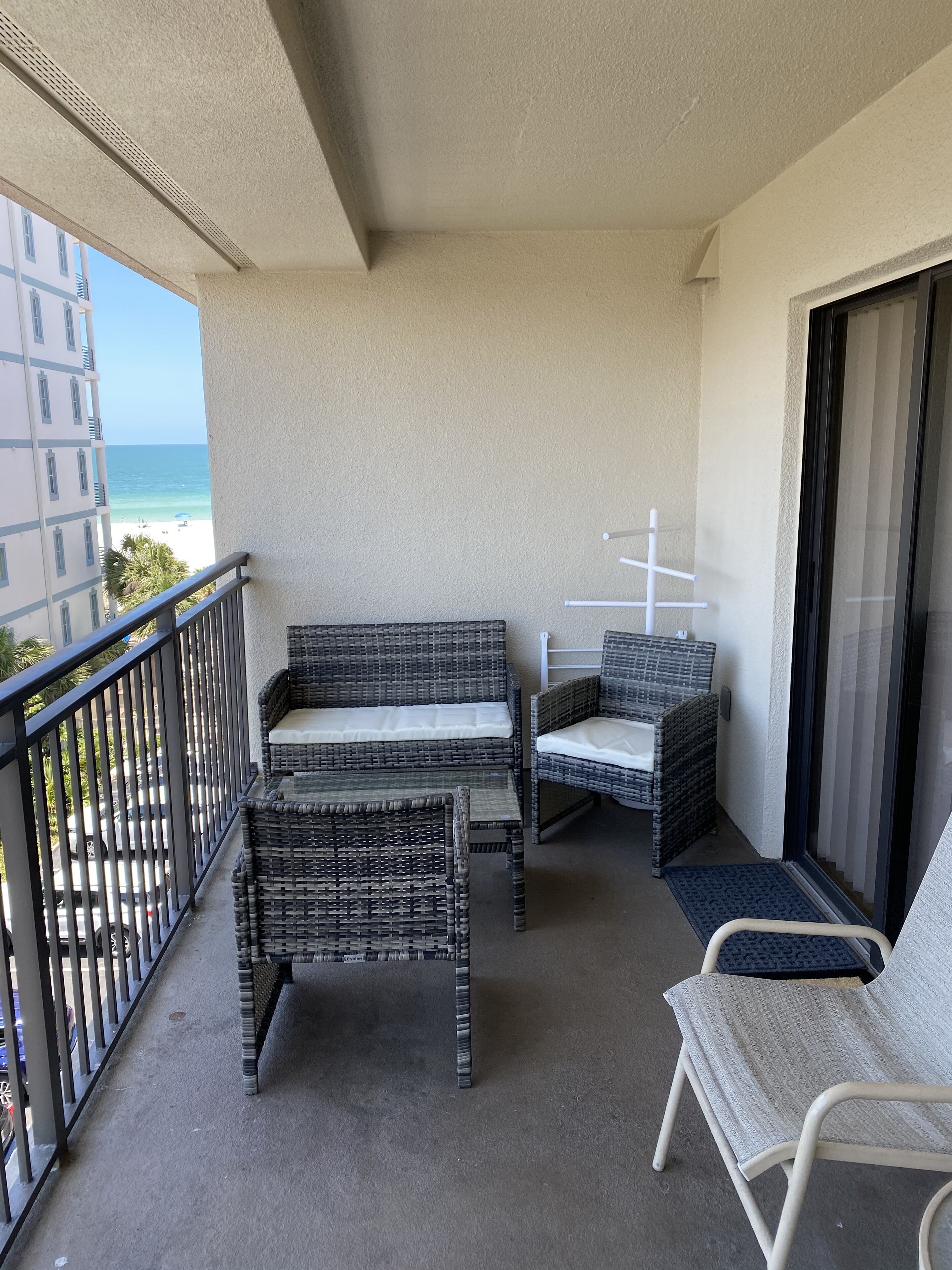 A balcony with wicker furniture, a view of the ocean, and a building in the background.