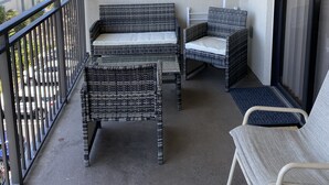 A balcony with wicker furniture, a view of the ocean, and a building in the background. - Modern Beach Condo ON  St. Pete Beach! (St. Pete Beach)