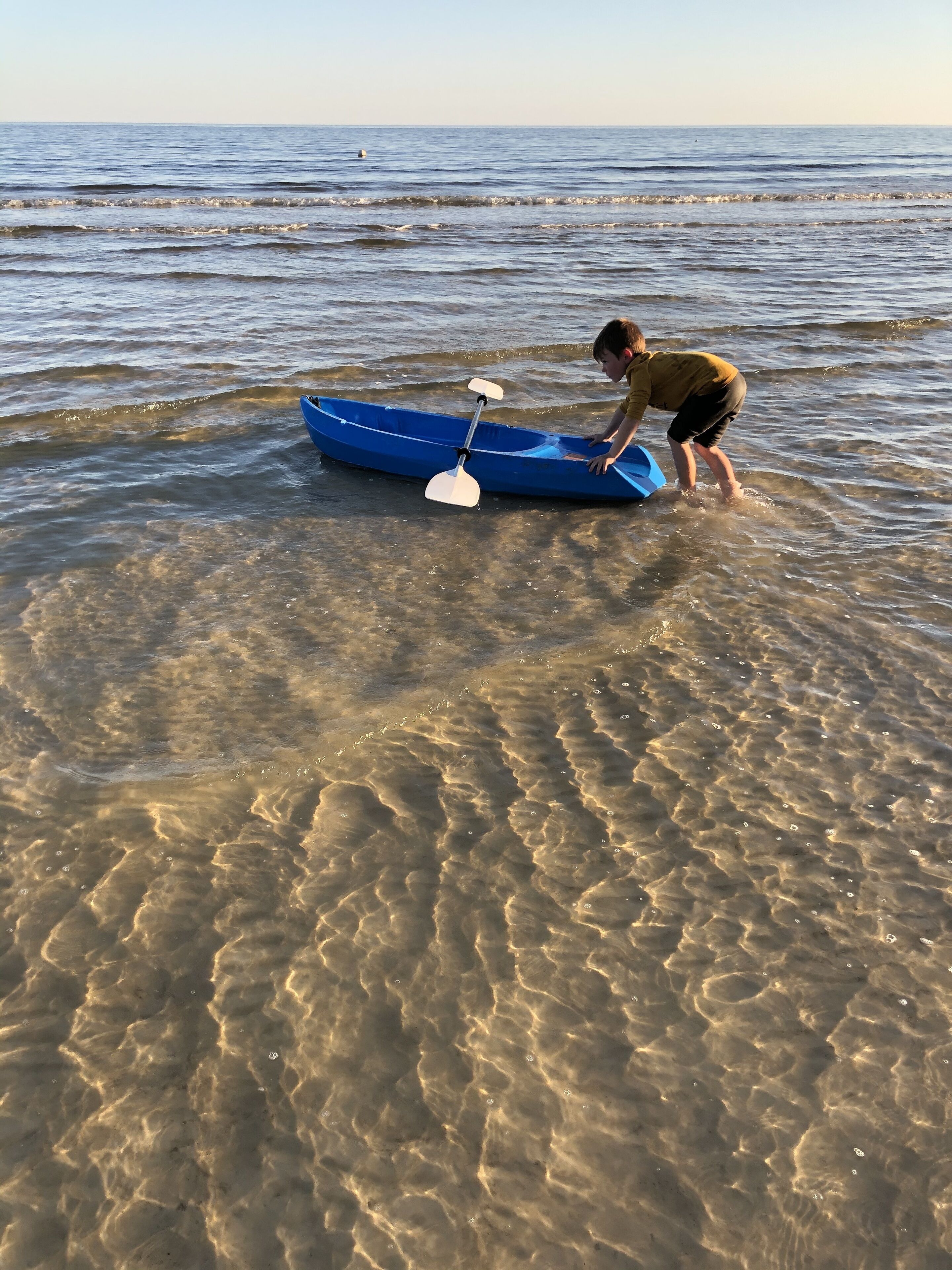 A person in a blue kayak on a beach with clear shallow waters.