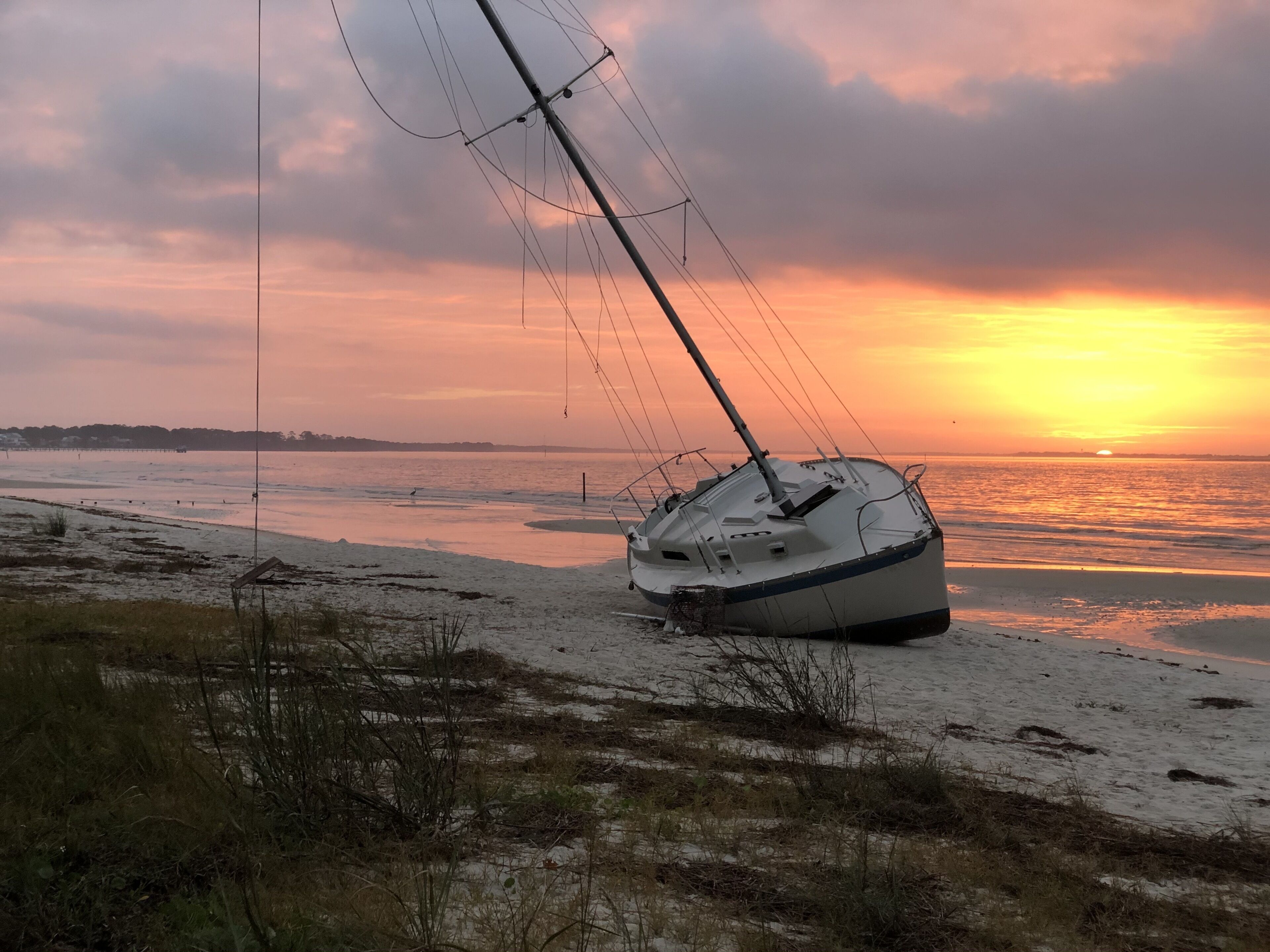 Ein Segelboot liegt gestrandet an einem Sandstrand, im Hintergrund ist ein Sonnenuntergang zu sehen.