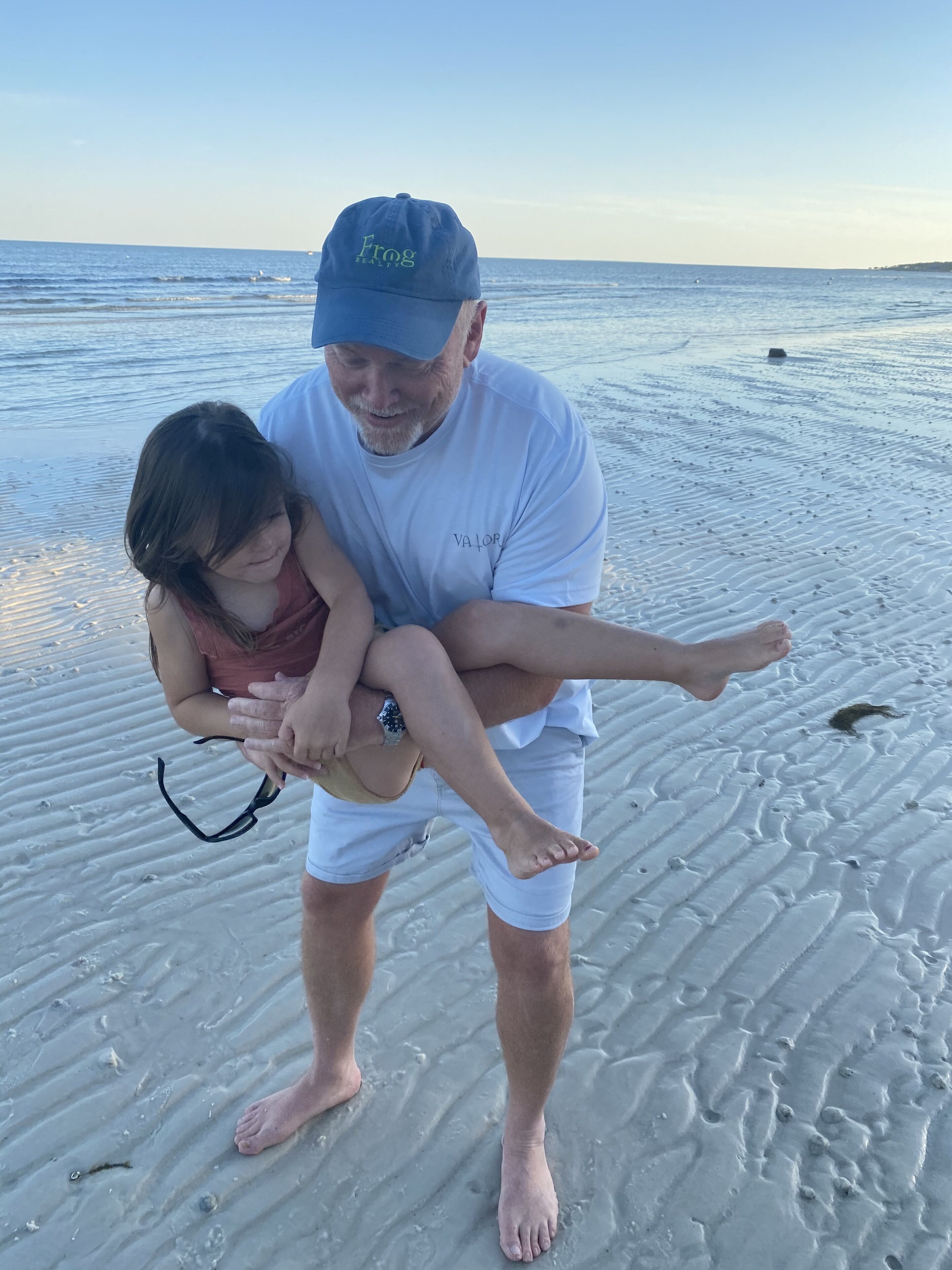 Un hombre lleva a un niño en una playa arenosa, con el océano al fondo.
