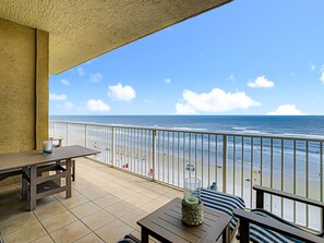 A balcony with a view of the beach, a table, and a chair.