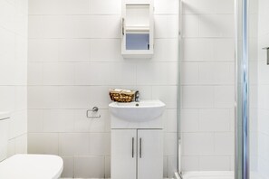 Bathroom features a white toilet, pedestal sink, and glass shower enclosure.