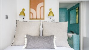 Ein Schlafzimmer mit einem Bett, zwei Wandlampen, einem gerahmten abstrakten Gemälde und einem durch eine offene Tür einsehbaren Badezimmer.