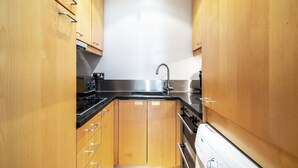 Eine kompakte Küche mit Holzschränken, einem Edelstahl-Spülbecken und einem eingebauten Backofen.