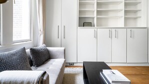 Ein modernes Wohnzimmer mit einem grauen Sofa, einem schwarzen Couchtisch und einer weißen Schrankwand mit vielen Fächern.