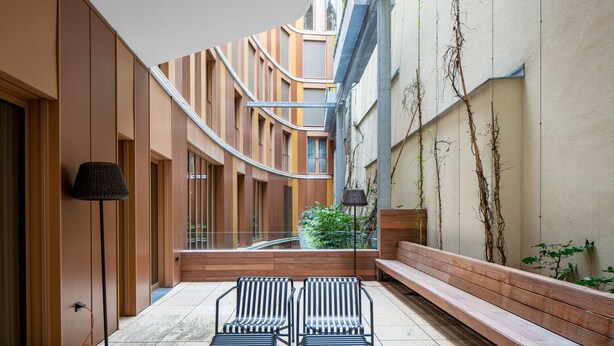 A modern courtyard with a curved staircase, wooden benches, and a glass railing. - Chic Innere Stadt 1BR w/ Gym & Doorman, walk to Graben, by Blueground (Vienna)