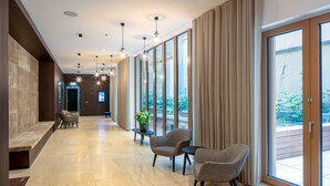 A modern hotel lobby with a long corridor, seating area, and large windows offering a view of the outdoors. - Chic Innere Stadt 1BR w/ Gym & Doorman, walk to Graben, by Blueground (Vienna)