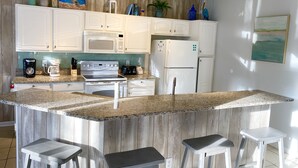 A modern kitchen with white cabinets, a granite countertop, a built-in oven, a microwave, a refrigerator, and a bar area with stools. - Mickey’s Vacation Villa-Premium- Minutes from Disney World with private pool! (Kissimmee)