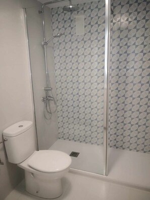 Une salle de bain comprenant des toilettes, un espace douche et un mur décoré d’un motif.