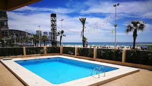 A rectangular swimming pool with a tiled deck, surrounded by a low wall and palm trees. - Levante Beach Jazmines Ac (Benidorm)