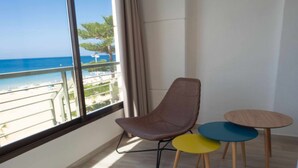 A room with a large window overlooking a beach, a brown chair, and two small round tables. - Levante Beach Jazmines Ac (Benidorm)