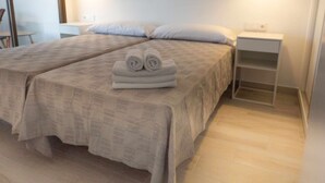 A double bed with a beige bedspread and two pillows, a small bedside table with a lamp, and a white nightstand with a shelf. - Levante Beach Jazmines Ac (Benidorm)