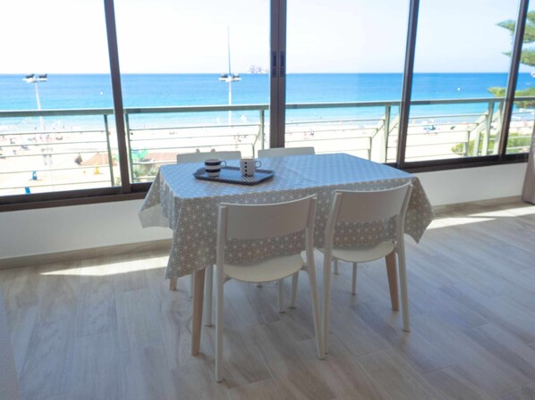 Un espace repas avec une table et des chaises, de grandes fenêtres offrant une vue sur la plage et l’océan.