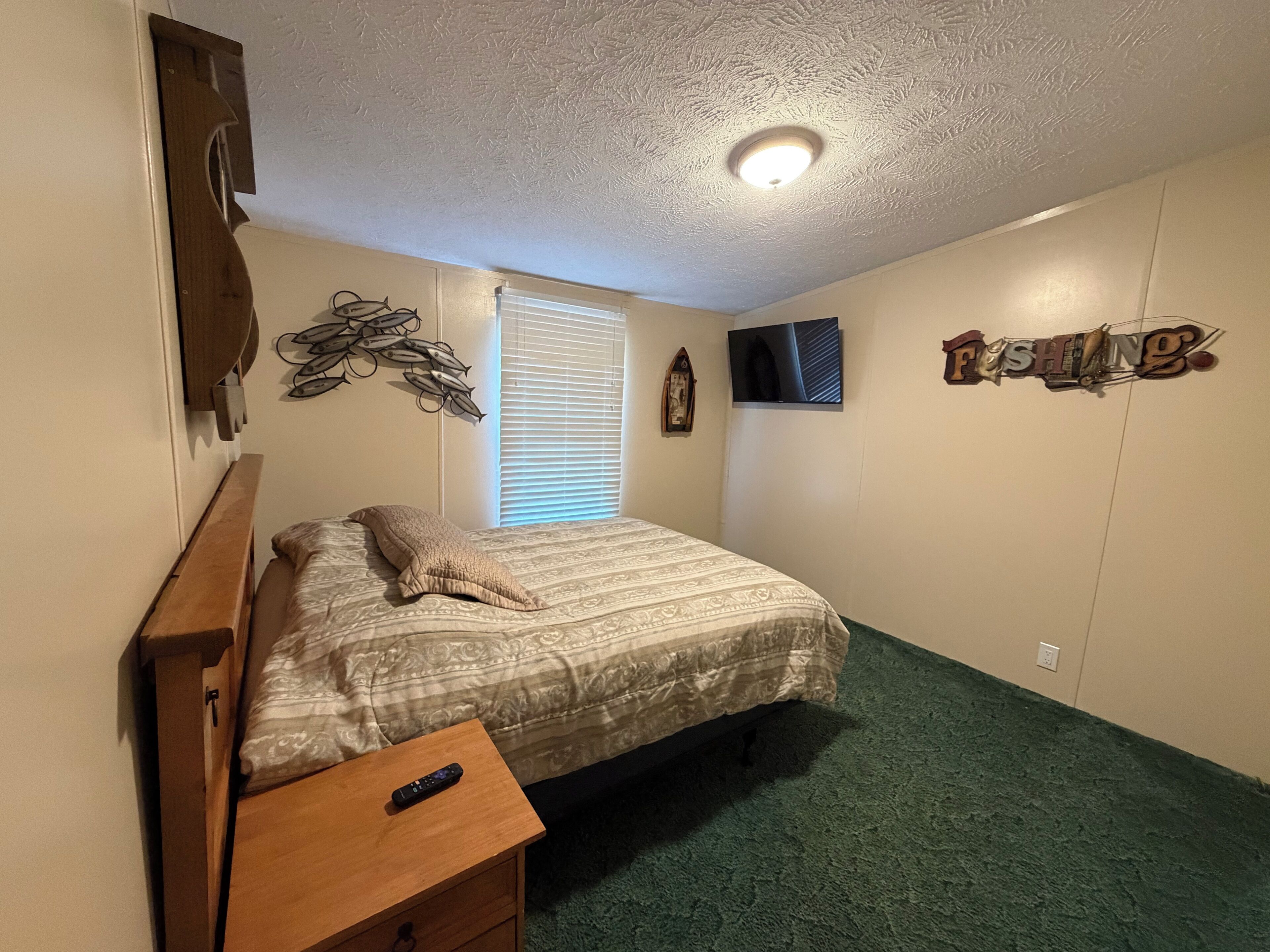 A bedroom with a bed, a nightstand, a TV, a wall clock, and a wall decoration.