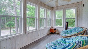 Una stanza con ampie finestre, una ventola a soffitto e una sedia in vimini con un cuscino decorato.