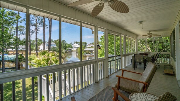 Un portico coperto con vista su un lago e alberi circostanti, con mobili in vimini e ventilatori a soffitto.