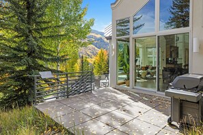A modern house with a patio, a grill, and a view of mountains.