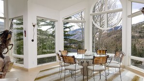 A dining area with a round table and six chairs, large windows offering mountain views, and a decorative horse sculpture.