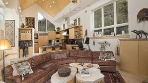 A spacious living area with a large brown leather sectional sofa, a coffee table, and a kitchen in the background.
