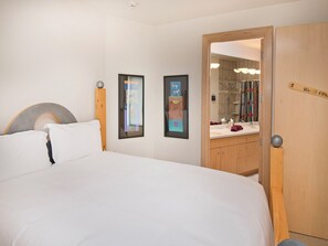 A hotel room with a bed, a wooden wardrobe, a bathroom with a mirror, and two framed pictures on the wall.