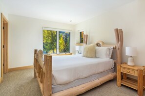 Un dormitorio con una ventana grande, una cama con estructura de madera, una mesita de noche con lámpara y un espejo.