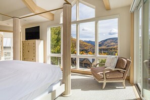 Une chambre avec un grand lit, une chaise, un téléviseur et une vue sur les montagnes grâce à de grandes fenêtres.
