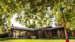 A modern house with a large glass front, a covered patio, and a well-maintained lawn. - Kaweah River House ~ Private River Access (Three Rivers)