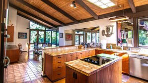 A spacious kitchen with wooden beams, large windows, and a central island with a built-in stove. - Kaweah River House ~ Private River Access (Three Rivers)