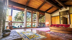 A spacious room with wooden beams, large windows, a stone wall, and a red sofa. - Kaweah River House ~ Private River Access (Three Rivers)