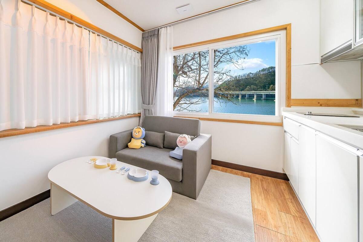 A compact room with a sofa, a small table, and a view of a lake through a window.