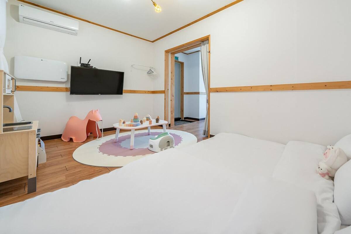 A hotel room with a large bed, a desk with a computer, a TV, and a children's play area.