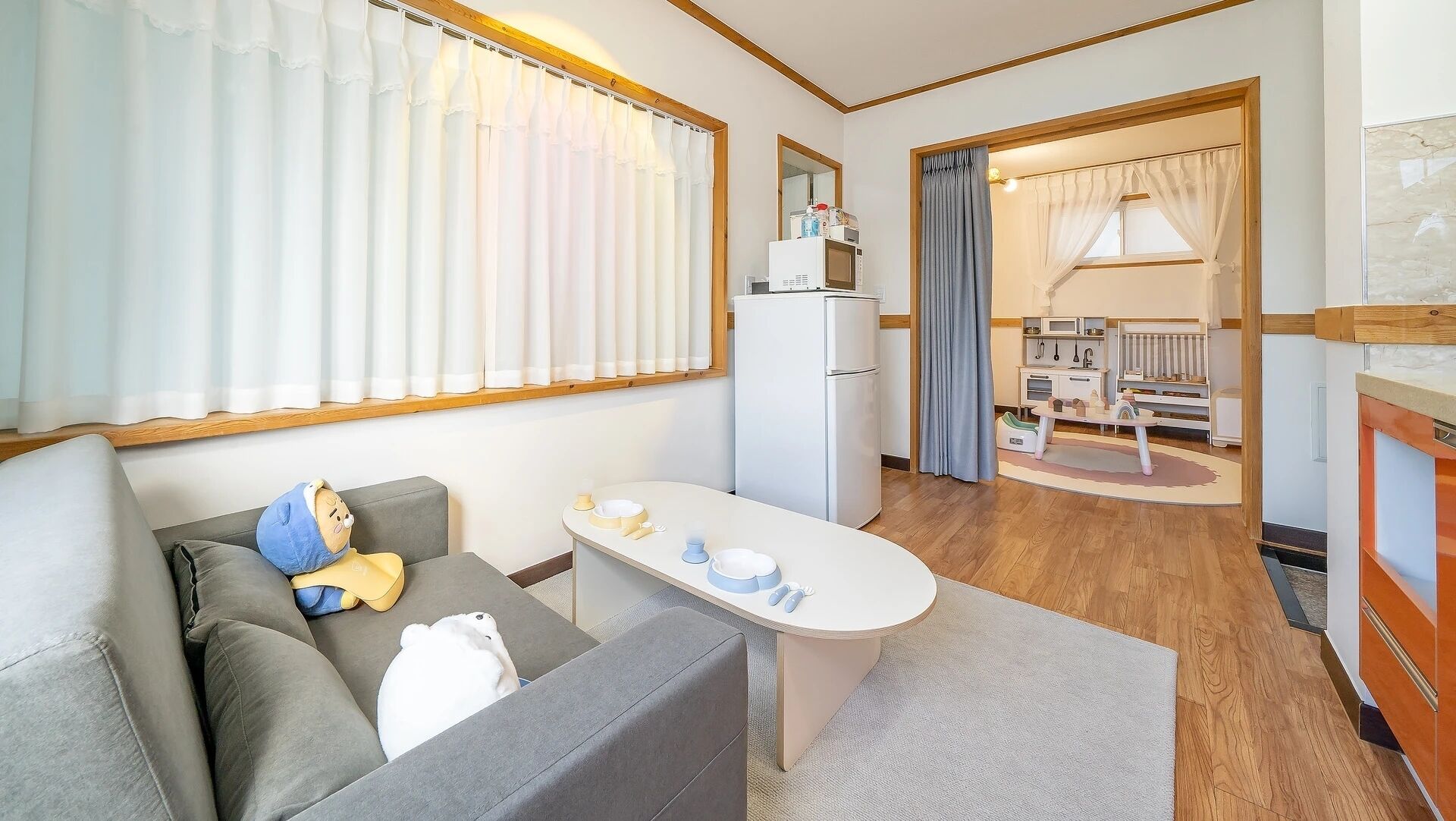 Un espacio habitable compacto con sofá, una mesita, kitchenette y área de juegos para niños.