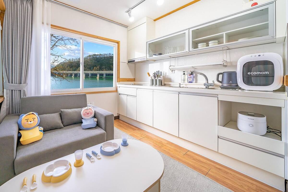A modern hotel room with a sofa, a dining table, and a kitchen area.
