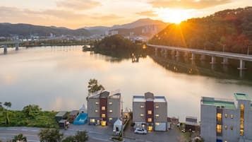 Un hotel a la orilla del río con arquitectura moderna, un puente al fondo y un atardecer.